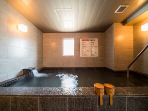 Zona de baño de aguas termales con pared de madera, suelo de baldosas y cartel que enumera los servicios.