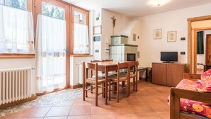 A room with a dining table, chairs, a television, a radiator, and a window with curtains.