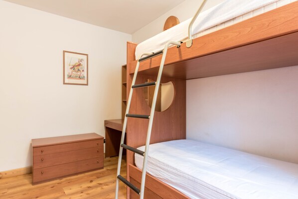 Un lit superposé avec une échelle, une commode en bois et un tableau encadré accroché au mur.