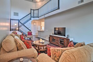 Un salon spacieux avec un plafond haut, un escalier et un téléviseur à écran plat.