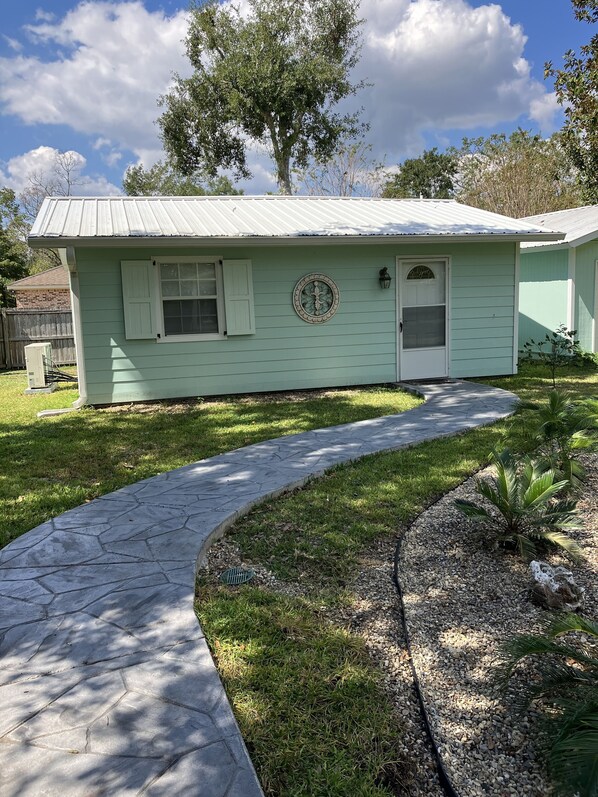A single-story house with a green exterior, a front door, and a window with shutters.