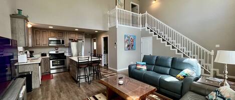 A spacious living room with a large sofa, a coffee table, and a staircase leading to an upper level.