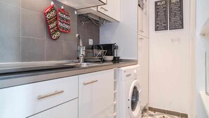 Una cocina moderna con armarios blancos, un lavamanos de acero inoxidable y una lavadora.