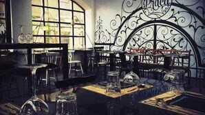 Un restaurante tenuemente iluminado con un amplio ventanal de arco y ornamentada rejería en la pared. Las mesas están dispuestas con copas y cubiertos.