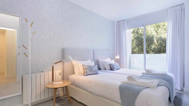 A modern hotel room with a large bed, bedside tables, and a view of the outdoors. - Tropical View Cascais - CheckinHome (Guincho)