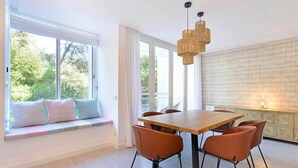 A dining area with a large table, six chairs, a bench with cushions, and a view of greenery outside. - Tropical View Cascais - CheckinHome (Guincho)