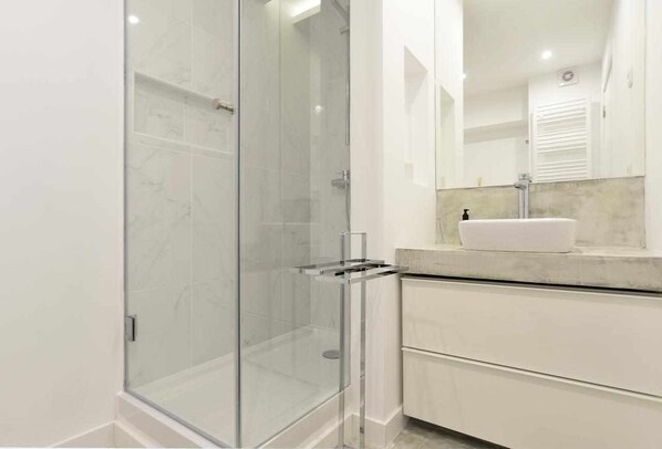 A modern bathroom with a glass shower enclosure, a white sink, and a marble countertop.