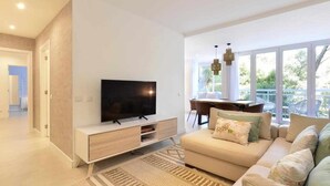 A modern living room with a flat-screen TV, a sofa, and a dining area with a table and chairs. - Tropical View Cascais - CheckinHome (Guincho)