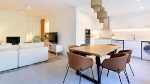 A modern living room with a sofa, TV, and dining area with chairs and a table. - Tropical View Cascais - CheckinHome (Guincho)
