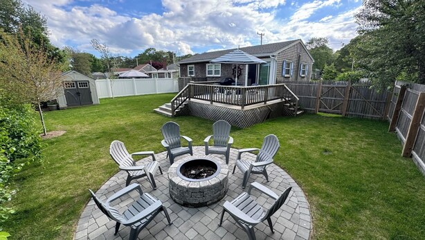 A backyard with a fire pit, outdoor seating, a wooden deck, and a house with a covered porch.