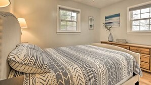 A bedroom with a bed, a ceiling fan, two windows, a dresser, and a lamp.
