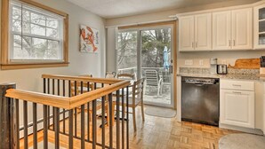 A kitchen with white cabinets, a dishwasher, and a dining area with a wooden table and chairs.