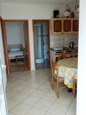 Una habitación compacta con cama, ducha y una pequeña cocina con mesa y sillas.