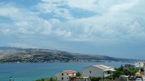 A coastal town with buildings along the waterfront, a clear sky, and mountains in the background. - Beautiful Coastline View Apartment a4 (Pag)