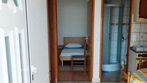 A room with a bed, a chair, a table with a tablecloth, and a door leading to another room. - Beautiful Coastline View Apartment a4 (Pag)