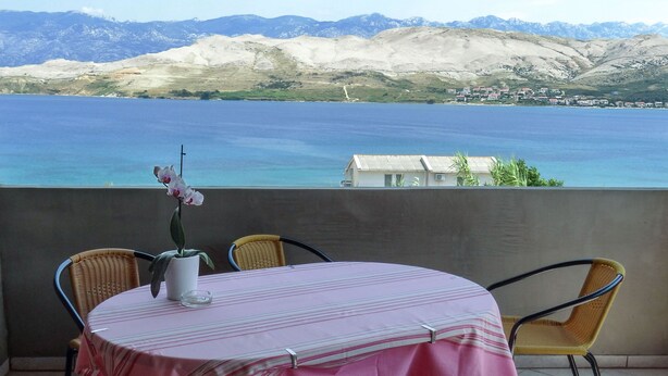 A round table with a striped tablecloth, wicker chairs, and a potted orchid. - Beautiful Coastline View Apartment a4 (Pag)