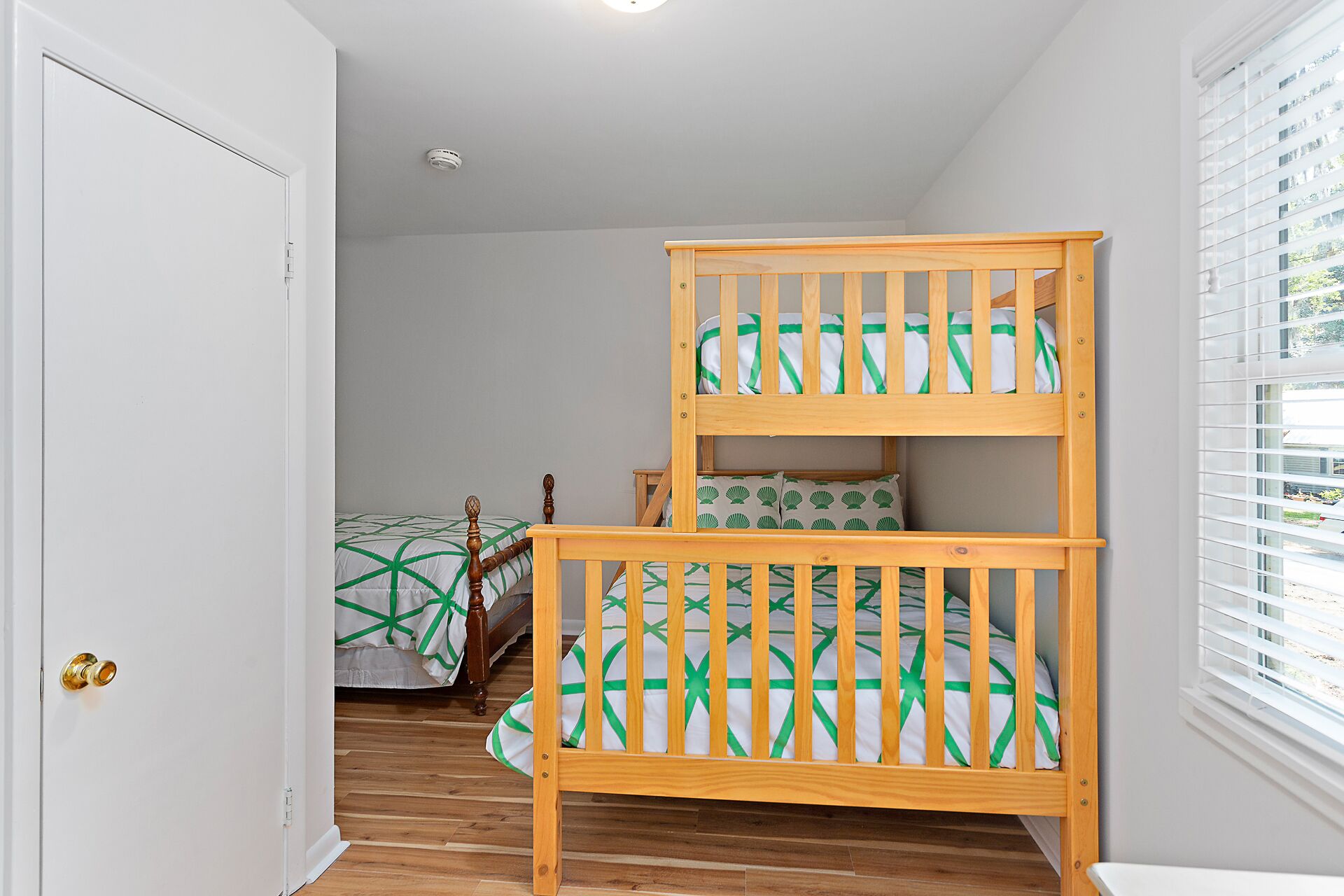 A room with a bunk bed, a door, and a window with blinds.
