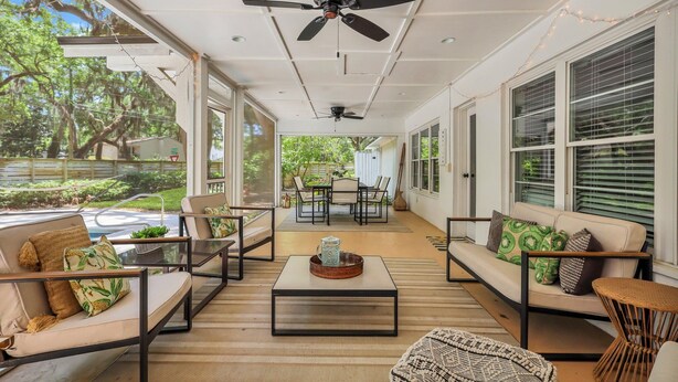 Eine großzügige Terrasse mit einer Couch, Stühlen und einem Couchtisch. Deckenventilatoren und große Fenster sind vorhanden.