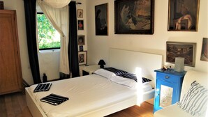Ein Schlafzimmer mit Bett, Nachttisch, Kommode und einem Fenster mit Vorhängen.