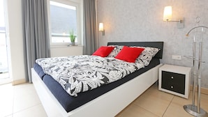 Une chambre à coucher moderne avec un grand lit, des rideaux gris, une petite table de chevet et une lampe sur pied.