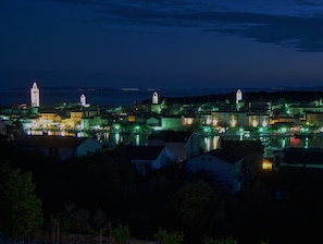 A coastal town at night with illuminated buildings and a prominent tower. - Apartment With View (Rab)