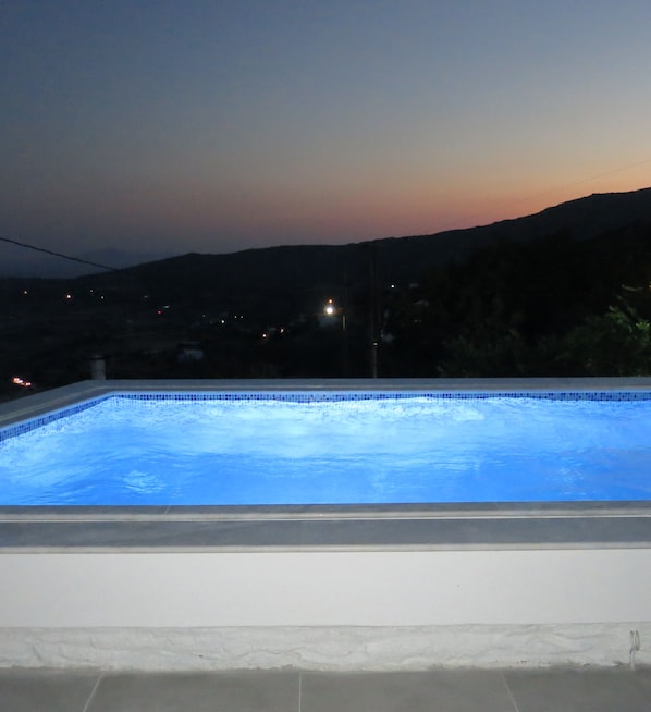 A swimming pool at dusk with a view of distant hills and a few lights in the background. - Room-andoni's House in Pitrofos Andros i (Andros)