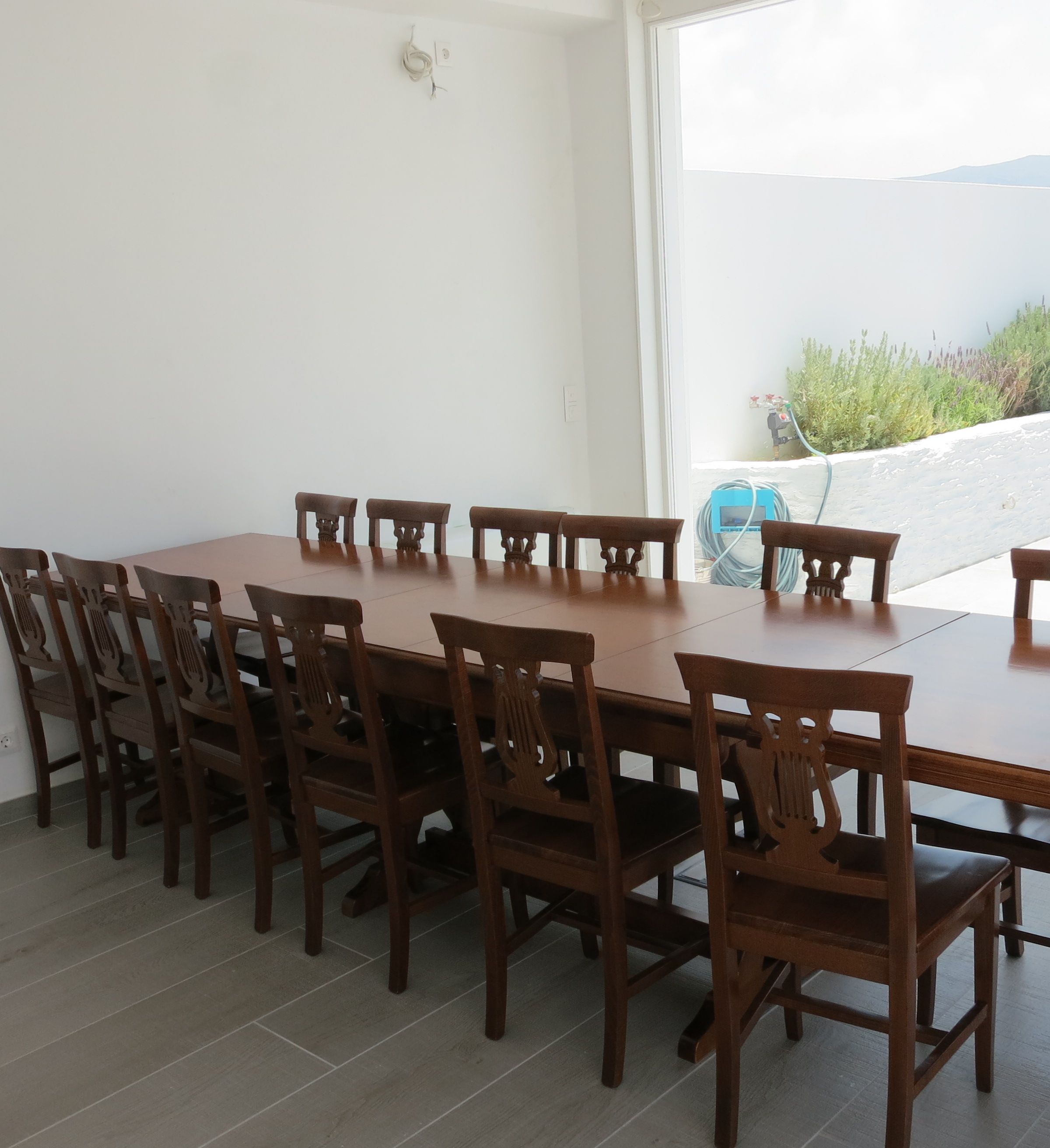 Un coin repas avec une longue table en bois et des chaises, une fenêtre donnant sur un beau paysage et un tuyau bleu fixé au mur.