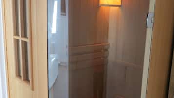 Uma sauna de madeira com porta de vidro, banco de madeira, mesa pequena e aquecedor fixado na parede.