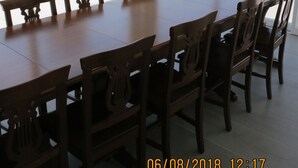 Un comedor con una larga mesa de madera y sillas, ventanas amplias con vistas a edificios y colinas.