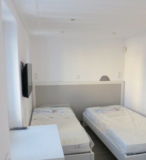 A room with two single beds, a small desk, and a TV mounted on the wall. - Room-andoni's House in Pitrofos Andros i (Andros)