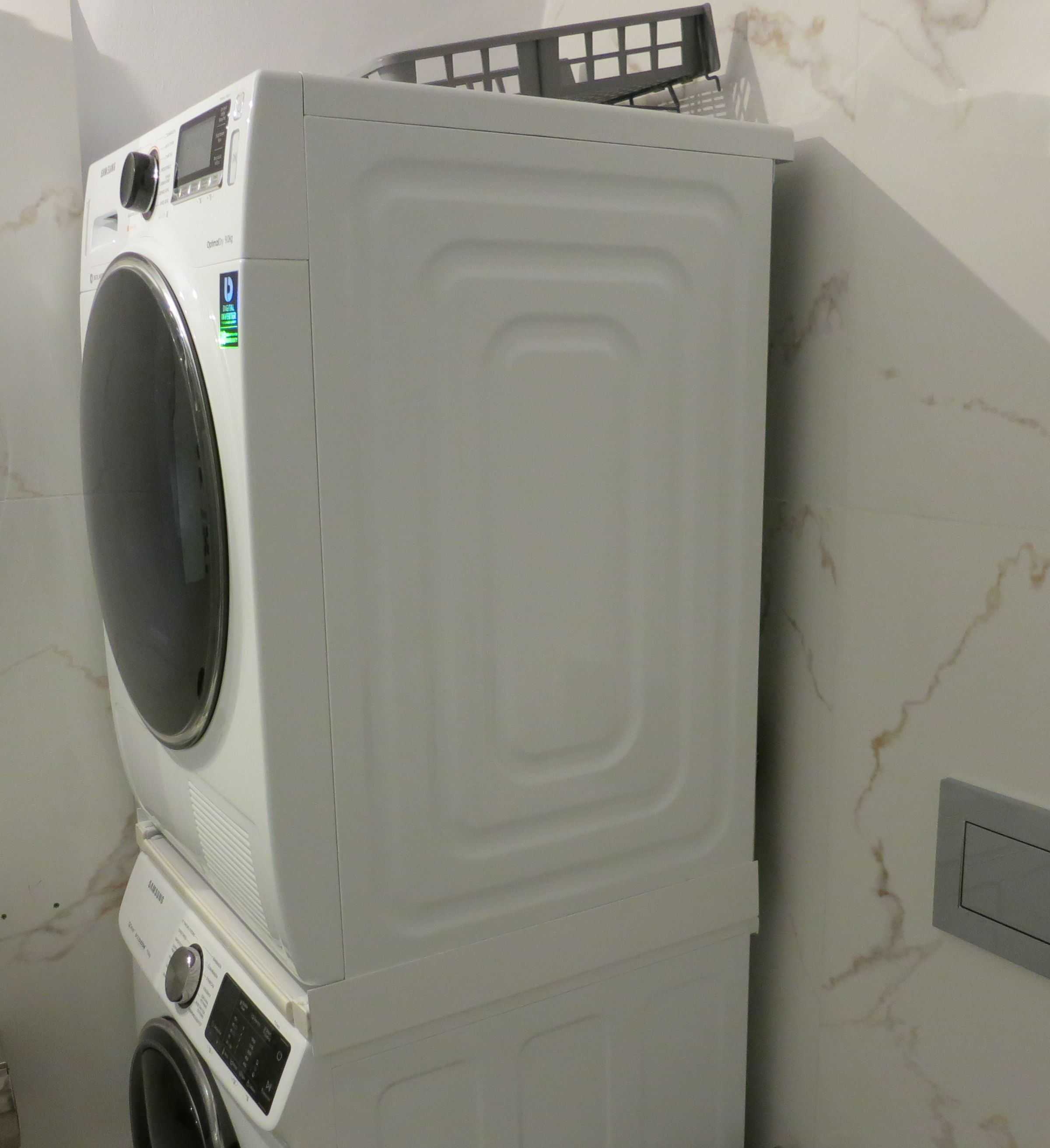 A stacked washer and dryer unit in a room with marble walls.