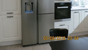 A modern kitchen with white cabinetry, a stainless steel refrigerator, an oven, and a coffee maker. - Room-andoni's House in Pitrofos Andros i (Andros)