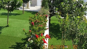 A white building with blue doors and windows, surrounded by green grass and trees. - Room-andoni's House in Pitrofos Andros i (Andros)