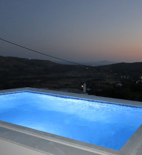 Una piscina rectangular con borde de azulejos, rodeada por una terraza blanca.