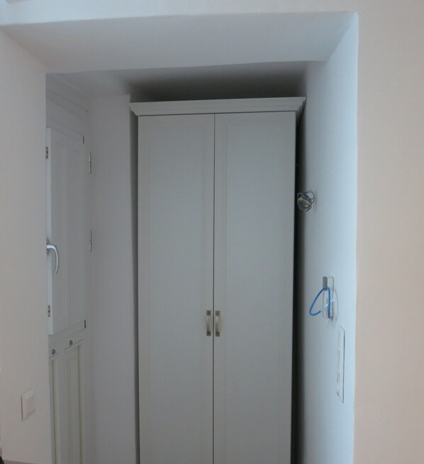 A white wardrobe with two doors, a light switch, and a power outlet on the wall.
