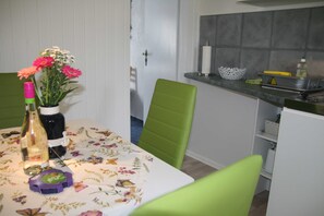 Un coin repas comprenant une table, des chaises, un vase avec des fleurs, une bouteille et un dessous de verre.