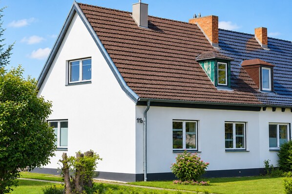 Une maison blanche avec un toit brun, de nombreuses fenêtres et le numéro « 11b » sur le côté.
