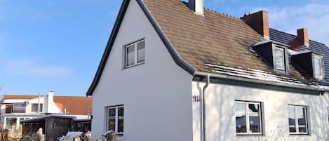 Een modern huis met twee verdiepingen, een schuin dak, een schoorsteen en een zichtbaar raam.