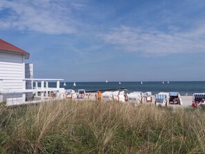 A beachside view with a white building, beach chairs, and a pier extending into the sea.