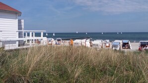 A beachside view with a white building, beach chairs, and a pier extending into the sea.