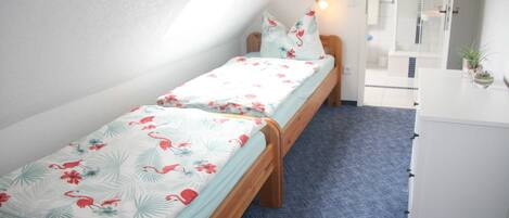 A bedroom with two single beds, a white dresser, and a shower area.