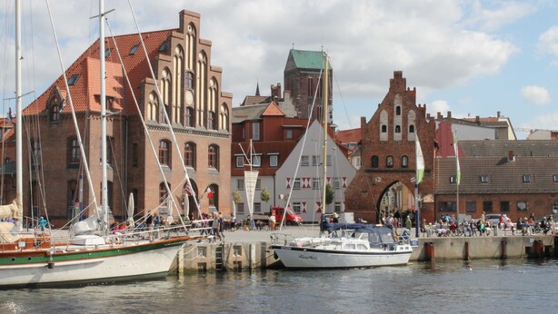 A waterfront with boats docked, a historic building with a red roof, and a large archway.