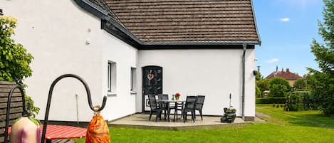 A white house with a tiled roof, a patio with a table and chairs, and a garden.