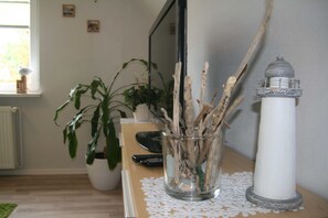 A room with a wooden table, a glass vase with sticks, a white lighthouse sculpture, a potted plant, and a television.