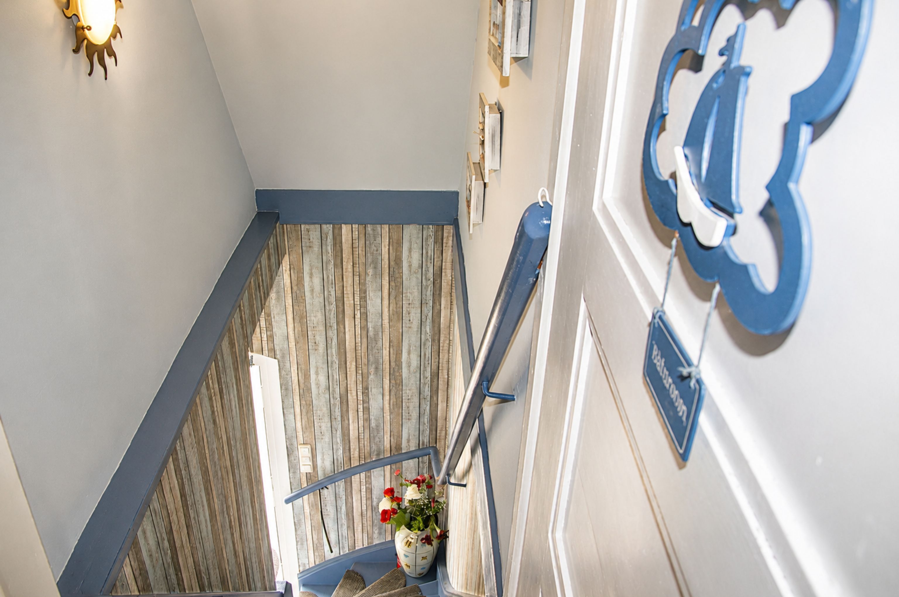 Una escalera con piso de madera, barandal azul y un cartel adosado a la pared.