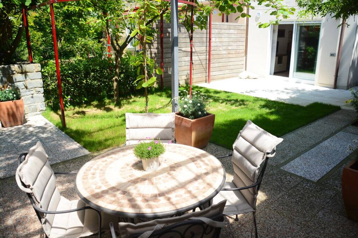 A patio with a round table and chairs, surrounded by potted plants and a small garden.