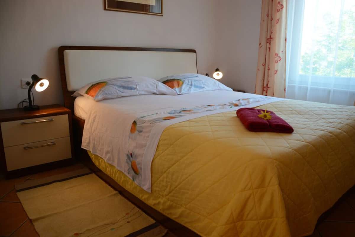 A neatly made bed with a yellow quilt, a bedside lamp, and a nightstand with drawers.