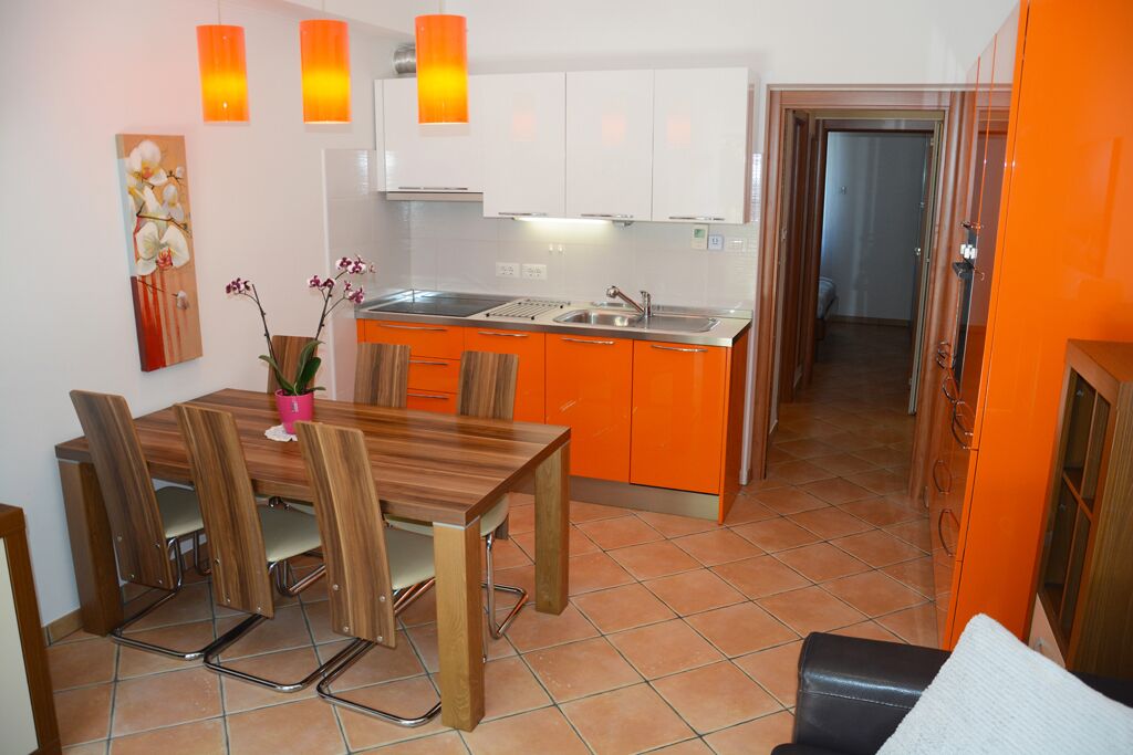 A compact kitchen with white cabinets, a wooden dining table with chairs, and orange accents.