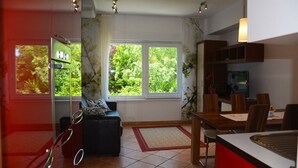 En moderne stue med sofa, spisebord og stole. Der er et vindue med udsigt til grøn natur.