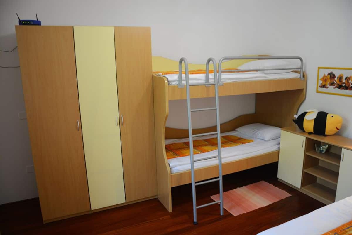 A bunk bed room with a wardrobe, a desk, and a stuffed toy.